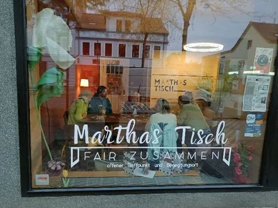 Zu sehen ist eine kleine Gruppe von Leuten, die gemeinsam im Cafe an einem Tisch sitzt.