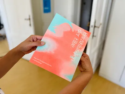 Zwei Hände halten ein Buch mit abstraktem, rot-blauem Cover und dem Titel 'Erzählungen der Elbe'