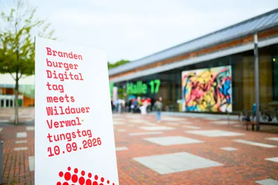 Weiße Informationstafel im Außenbereich vor der Halle 17 auf dem Campus der TH Wildau. Auf der Tafel steht in roter Schrift: „Brandenburger Digitaltag meets Wildauer Verwaltungstag 10.09.2026“.