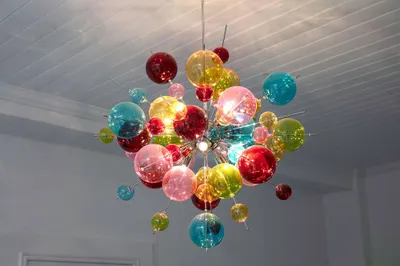 Das Foto zeigt einen Kronleuchter, der aus verschiedenfarbigen, unterschiedlich großen Glaskugeln besteht, die sternförmig angeordnet sind.