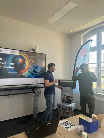 Zwei Personen stehen in einem Konferenzraum vor einem Smartboard. Eine der beiden Personen testet eine VR-Brille.